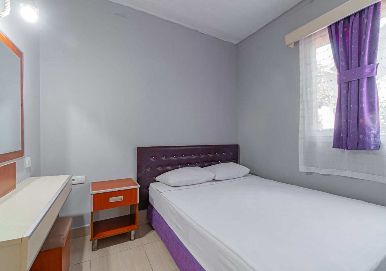 A bedroom with a bed, a nightstand, a desk, and a window with curtains.