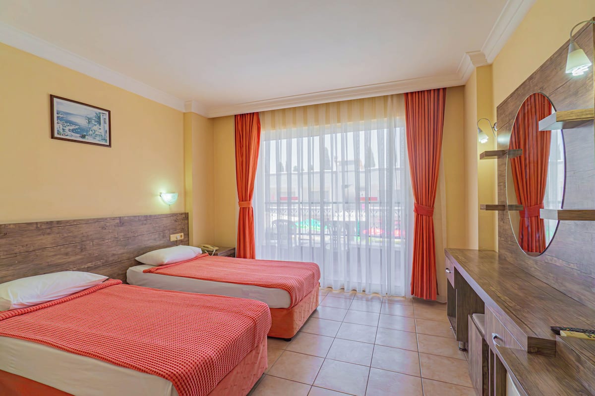 A hotel room with two beds, a wooden headboard, a large window with curtains, a mirror, and a TV.