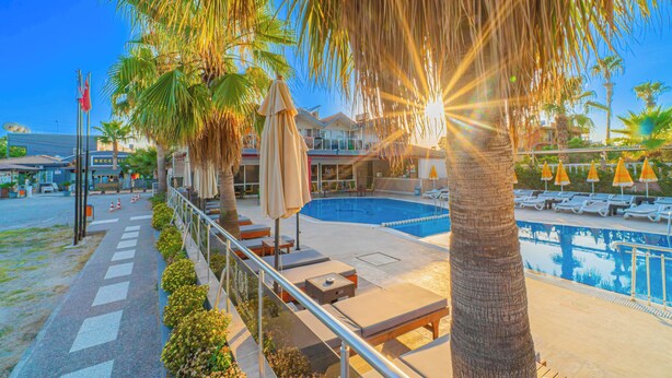 A poolside area with lounge chairs and umbrellas, a clear sky, and a building in the background. - Sayanora Hotel- All Inclusive (Manavgat)
