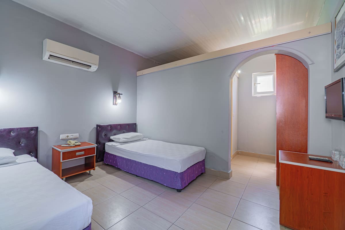 A hotel room with two beds, a wooden nightstand, a desk, an air conditioner, and a small window.