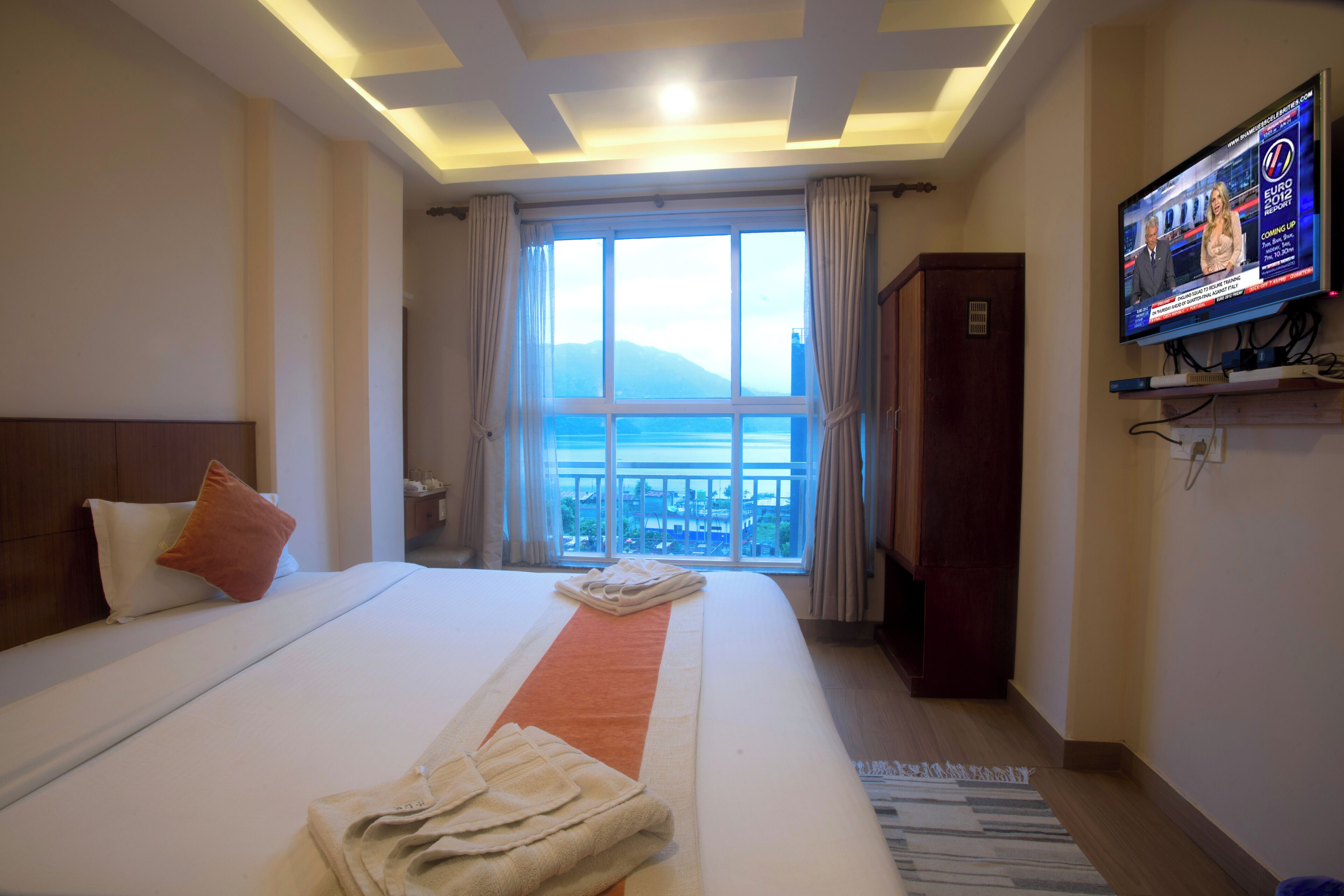A hotel room with a large bed, a TV on the wall, and a view of the sea through the window.