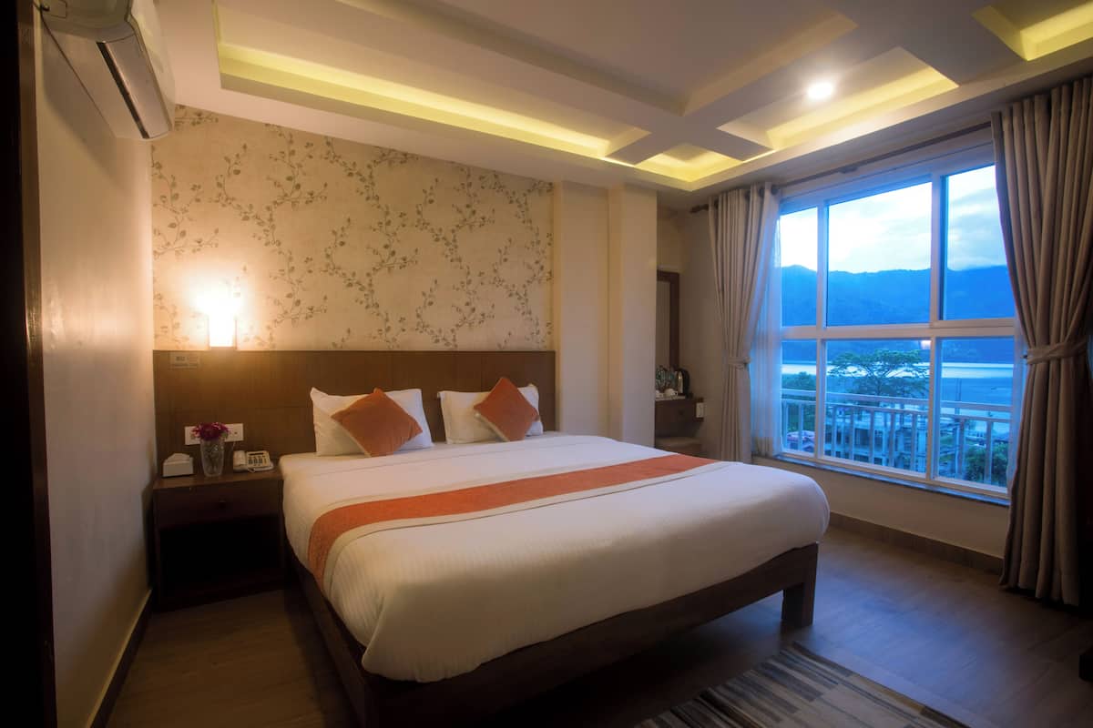 A hotel room with a large bed, a nightstand, a wall-mounted lamp, and a window with curtains.