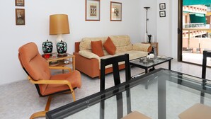 A modern living room with a sofa, armchairs, a glass coffee table, and a floor lamp. - Seafront Apartment with Parking in Torredembarra (Torredembarra)