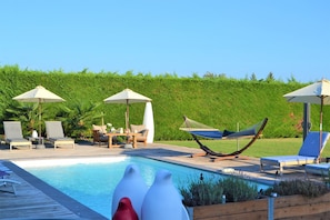 A pool area with lounge chairs, umbrellas, and a hammock.