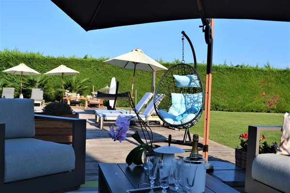 A deck with outdoor seating including lounge chairs, a hanging chair, and umbrellas.