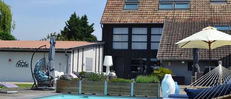 A swimming pool with lounge chairs and umbrellas, a wooden deck, and a two-story building with a tiled roof.