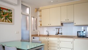 Una cocina moderna con una mesa de comedor de vidrio y sillas grises, armarios blancos y un microondas.