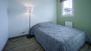 Une chambre à coucher avec un lit, une lampe sur pied, une fenêtre donnant sur les montagnes et un radiateur.