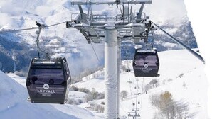 Un télésiège avec des cabines portant l’inscription « SKYVAL », situé dans une région montagneuse enneigée.