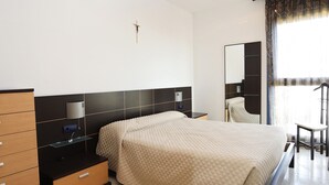 A hotel room with a bed, a dresser, a nightstand, a lamp, a mirror, and a window with curtains.