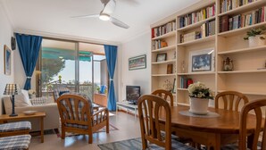 A cozy living room with a dining area, a bookshelf, and a ceiling fan. - Beachfront Apartment with Terrace and Private Parking (Torredembarra)