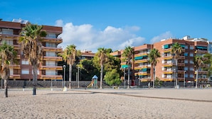 A sandy beach with palm trees and a playground. In the background, there are multi-story buildings with balconies. - Beachfront Apartment with Terrace and Private Parking (Torredembarra)