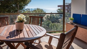 A wooden table and chairs on a balcony with a view of the sea and trees. - Beachfront Apartment with Terrace and Private Parking (Torredembarra)