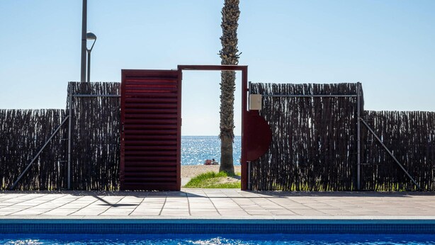 A swimming pool with a wooden fence and a gate, leading to a beach. - Beachfront Apartment with Terrace and Private Parking (Torredembarra)