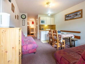 A compact room with a kitchenette, a dining area with a table and chairs, and a bed with a patterned blanket.