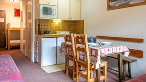 Cocina compacta con microondas, estufa y refrigerador. Hay una mesa de comedor con sillas y un cuadro en la pared.