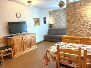 A cozy living room with a television, wooden furniture, a sofa, and a brick wall. - Central 2* studio with balcony and WiFi (Chamonix-Mont-Blanc)