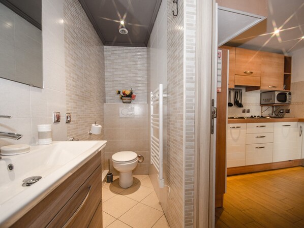 A modern bathroom with a white sink, toilet, and shower. It features a wooden vanity, a mirror, and a small flower arrangement on the wall. - Central 2* studio with balcony and WiFi (Chamonix-Mont-Blanc)
