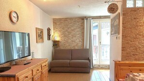 Ein gemütliches Wohnzimmer mit Fernseher, einer Couch, Holzschränken und einer Steinwand.
