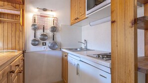 A compact kitchen with wooden cabinets, a white countertop, a stainless steel sink, and a microwave.