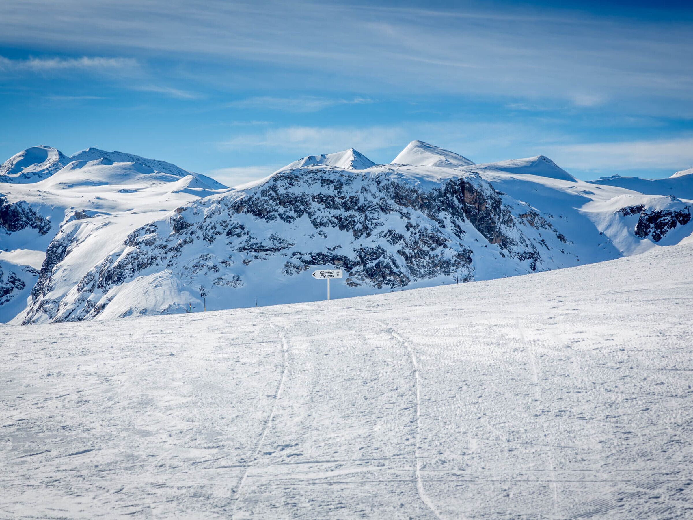 A snow-covered mountain with a ski trail and a sign indicating a ski run.
