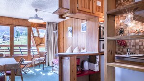 A cozy cabin interior with a dining area, kitchen, and large windows offering a scenic view. - 3-room apartment ski-in ski-out, 6 pers., south, La Daille (Val-d'Isère)