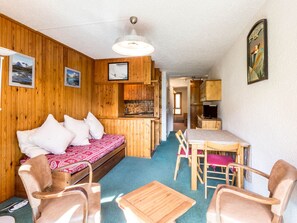 A cozy cabin-style room with a wooden interior, a bed with patterned bedding, a dining table with chairs, and a kitchen area.