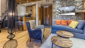 A modern living room with a stone wall, a blue sofa, and a wooden coffee table. - Luxury Apartment with WiFi and Parking, Ski-in/Ski-out, Town Center (Val-d'Isère)