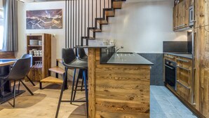 A modern kitchen with wooden accents, a bar area, and a dining space with chairs and a table. - Luxury Apartment with WiFi and Parking, Ski-in/Ski-out, Town Center (Val-d'Isère)