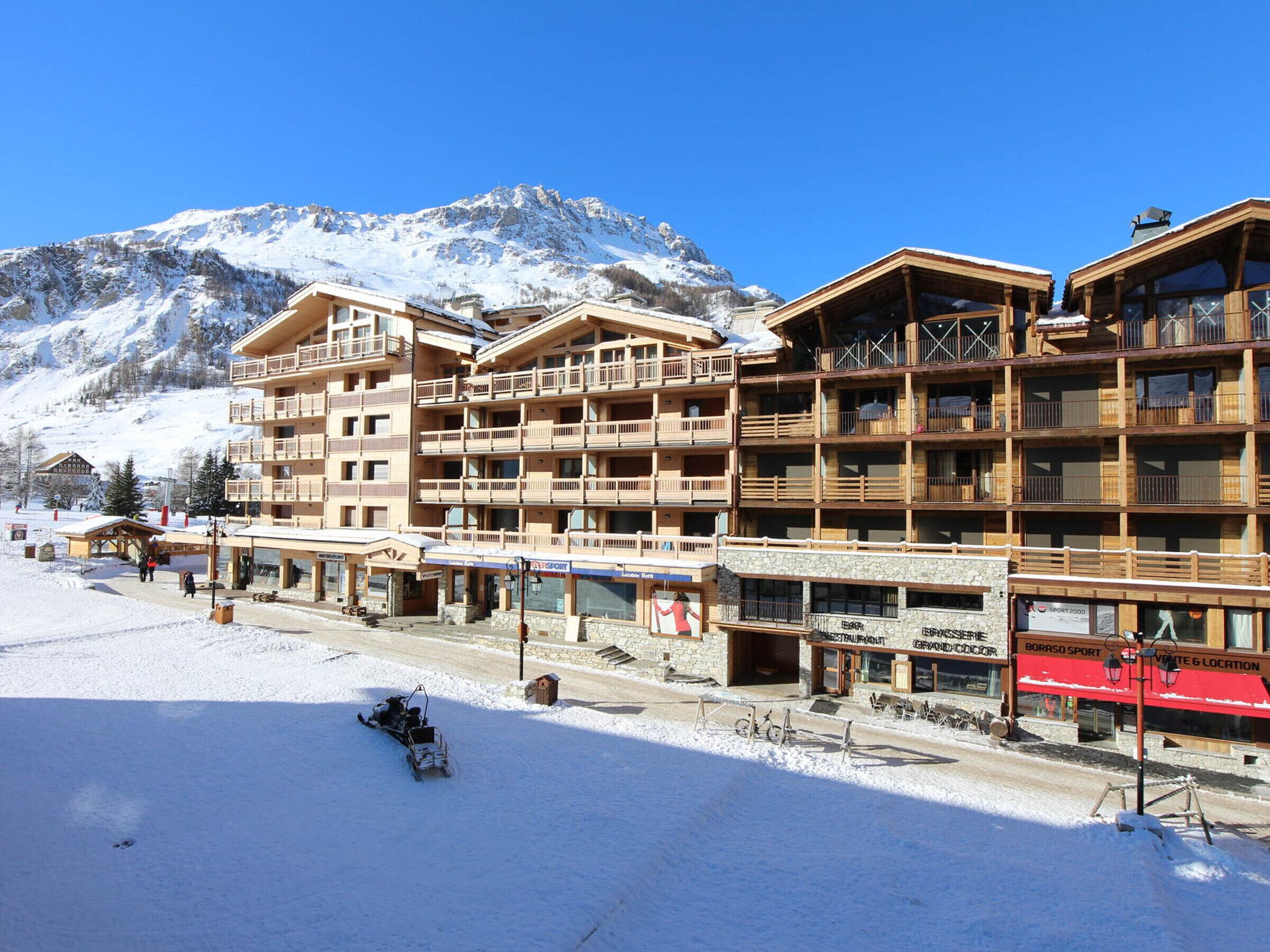 Un hotel a più piani con balconi, una seggiovia e uno scenario montano.