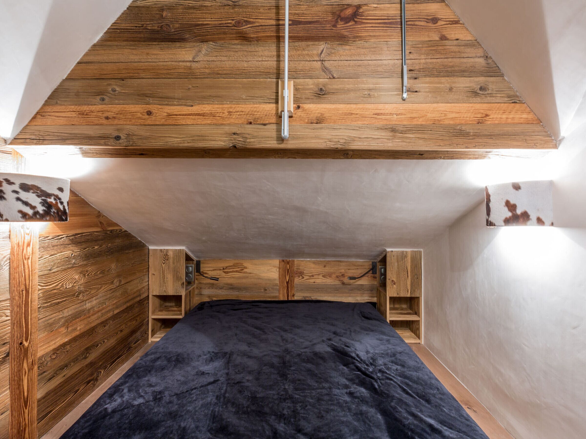 A compact bedroom with a sloped ceiling, wooden walls, and a black bedspread.