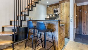 A modern kitchen with a wooden island, bar stools, a built-in microwave, and a staircase with black railings. - Luxury Apartment with WiFi and Parking, Ski-in/Ski-out, Town Center (Val-d'Isère)