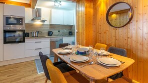 A modern kitchen with built-in appliances, a dining table set for four, and a large mirror on the wall. - Elegant apartment with WiFi, central location, ski-in/ski-out, parking, balcony, and elevator access (Val-d'Isère)