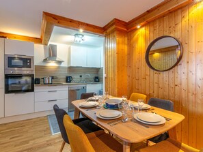 A modern kitchen with built-in appliances, a dining table set for four, and a large mirror on the wall. - Elegant apartment with WiFi, central location, ski-in/ski-out, parking, balcony, and elevator access (Val-d'Isère)