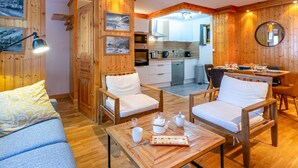 A cozy room with a wooden interior, a dining area with a table set for two, and a kitchen visible through an open door. - Elegant apartment with WiFi, central location, ski-in/ski-out, parking, balcony, and elevator access (Val-d'Isère)