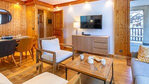 A cozy room with wooden walls, a dining area, a sofa, a TV, and a view of a snowy landscape. - Elegant apartment with WiFi, central location, ski-in/ski-out, parking, balcony, and elevator access (Val-d'Isère)