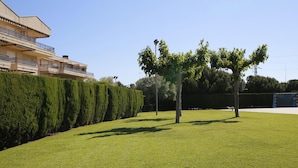 Un'area verde curata con siepi e alberi ben potati, cielo sereno e un edificio con balconi sullo sfondo.