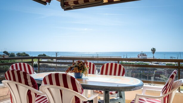 Una terrazza con un tavolo rotondo e sedie a righe, con vista sulla costa.