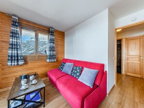 A red sofa with patterned pillows, a wooden table with cups and a kettle, and a window with curtains. - Apartment with Southwest balcony, garage, pets allowed (Val-d'Isère)