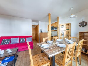A dining area with a wooden table set for four, surrounded by wooden chairs, and a red sofa with patterned cushions. - Apartment with Southwest balcony, garage, pets allowed (Val-d'Isère)