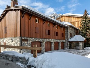 A wooden building with stone walls and multiple doors, surrounded by snow.
