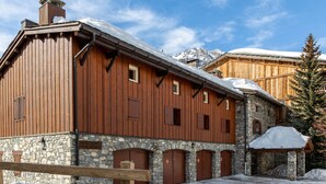 A wooden building with stone walls and multiple doors, surrounded by snow and mountains in the background. - Rustic Duplex Apartment with Large South-Facing Terrace Near Val-d'Isère Village (Val-d'Isère)