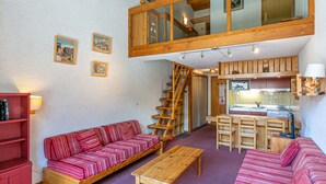 A cozy interior with a wooden staircase, a sofa, a dining table, and a kitchen area. - Rustic Duplex Apartment with Large South-Facing Terrace Near Val-d'Isère Village (Val-d'Isère)
