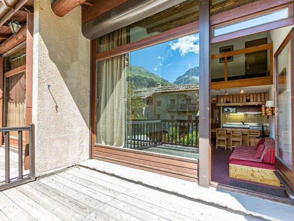 A wooden balcony with a view of mountains, a wooden interior with a bed and a kitchen area.