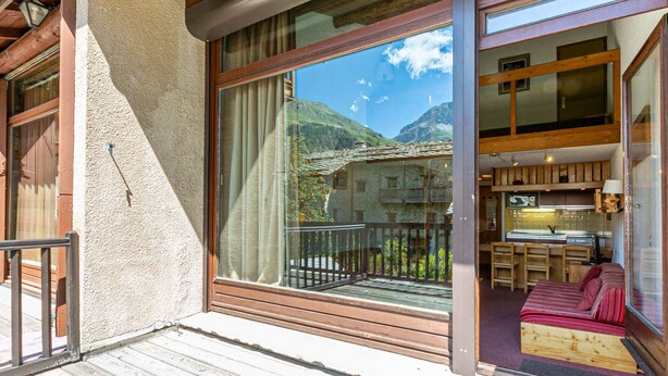 A wooden balcony with a view of mountains, a wooden interior with a bed and a kitchen area. - Rustic Duplex Apartment with Large South-Facing Terrace Near Val-d'Isère Village (Val-d'Isère)