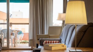 A modern living room with a sofa, a table with a lamp, and a view of the outside through a glass door. - Seaside apartment with air conditioning and private parking (Torredembarra)
