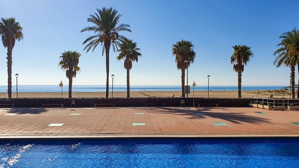 A swimming pool with a view of the beach and palm trees. - Seaside apartment with air conditioning and private parking (Torredembarra)