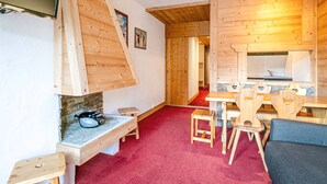 Un intérieur chaleureux en bois, avec un téléviseur fixé au mur, une cheminée en pierre, un coin repas avec des chaises en forme de cœur et une cuisine avec un dosseret carrelé.