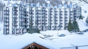 Un hôtel moderne à plusieurs étages, doté de balcons, qui se dresse sur un paysage montagneux enneigé.