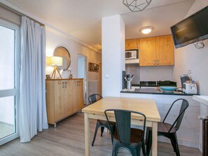Eine moderne Küche mit Holzschränken, einem Esstisch und Stühlen. Ein Fernseher ist an der Wand befestigt und ein Fenster mit Vorhängen vorhanden.